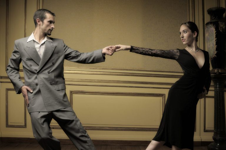 Mann in grauem Anzug und Frau in schwarzem Kleid tanzen miteinander